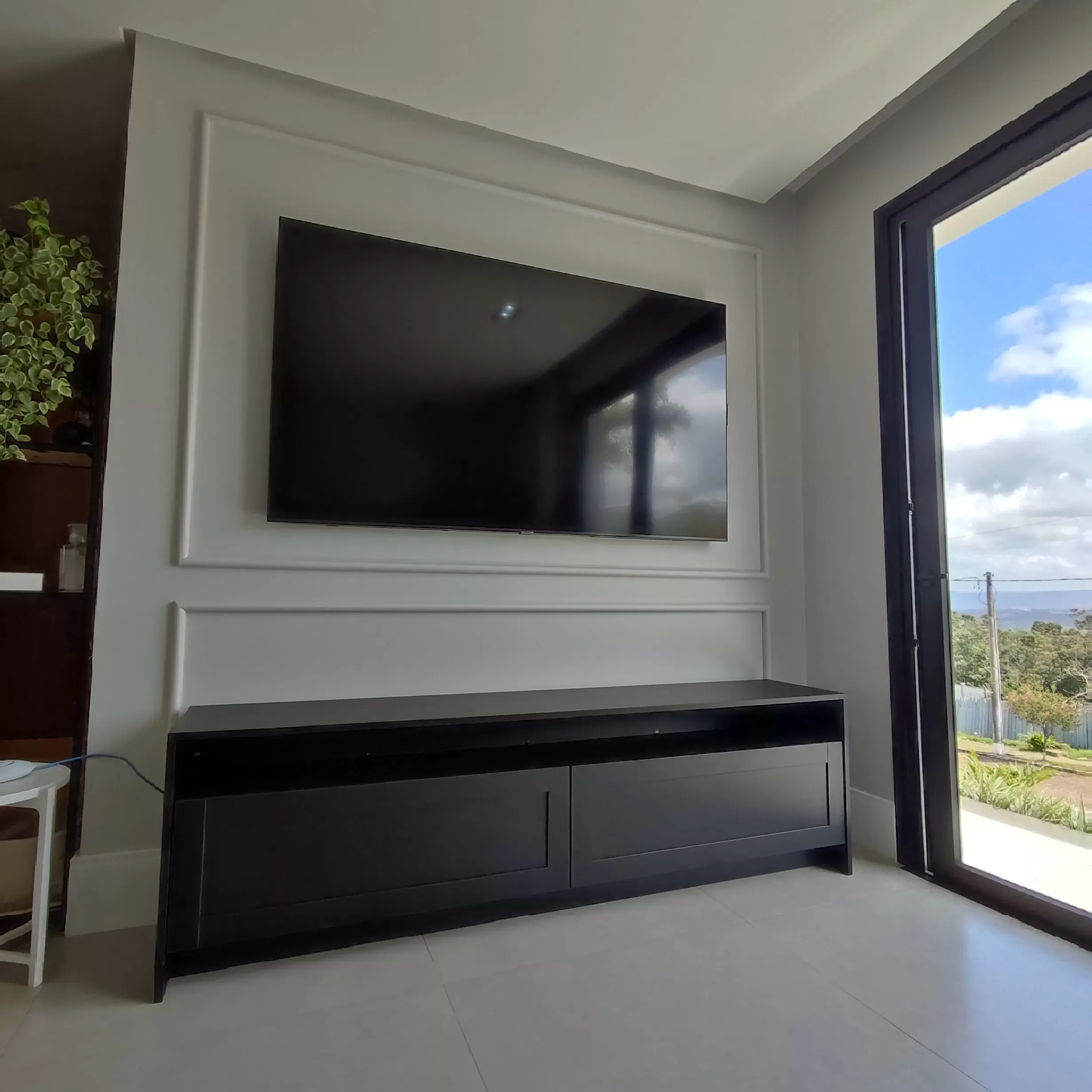 Painel de TV planejado com rack suspenso preto e detalhes em madeira, instalado profissionalmente.